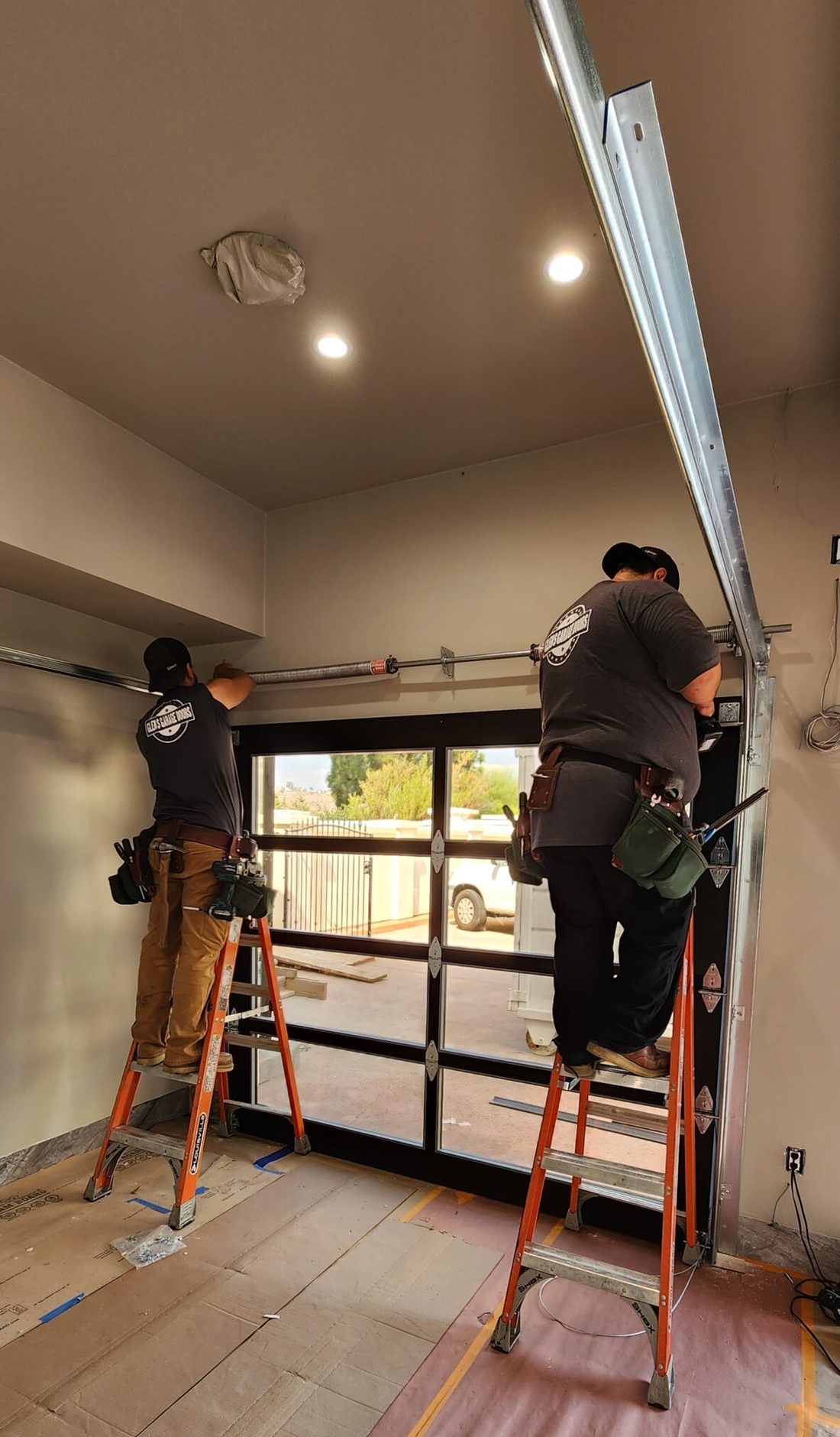 Two Glen's technicians on ladders fitting a full-view garage door